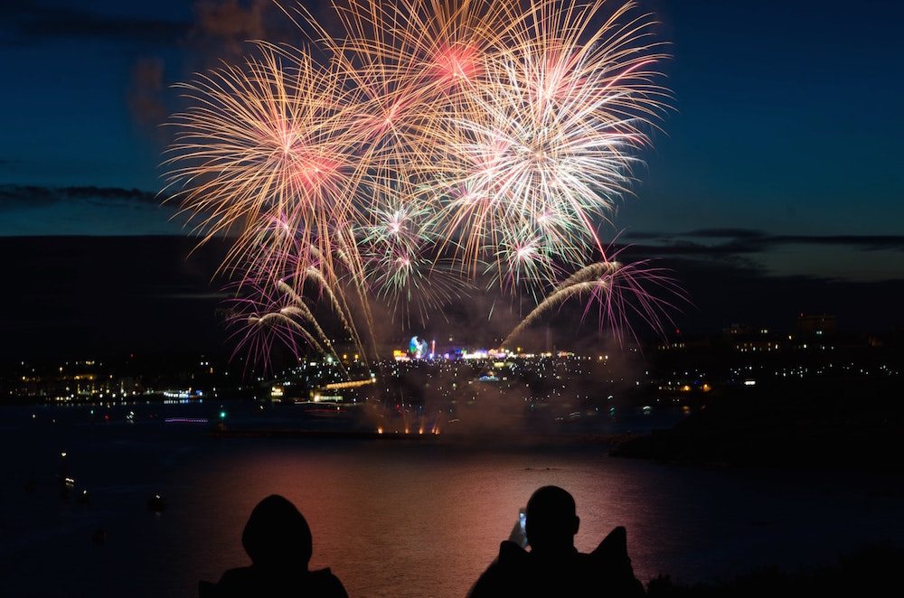 Silhouette of two people taking pictures of fireworks at night.