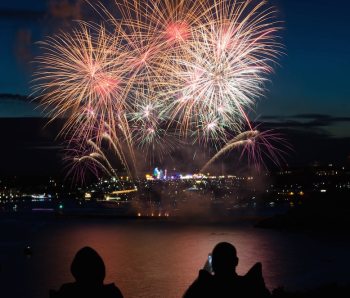Silhouette of two people taking pictures of fireworks at night.